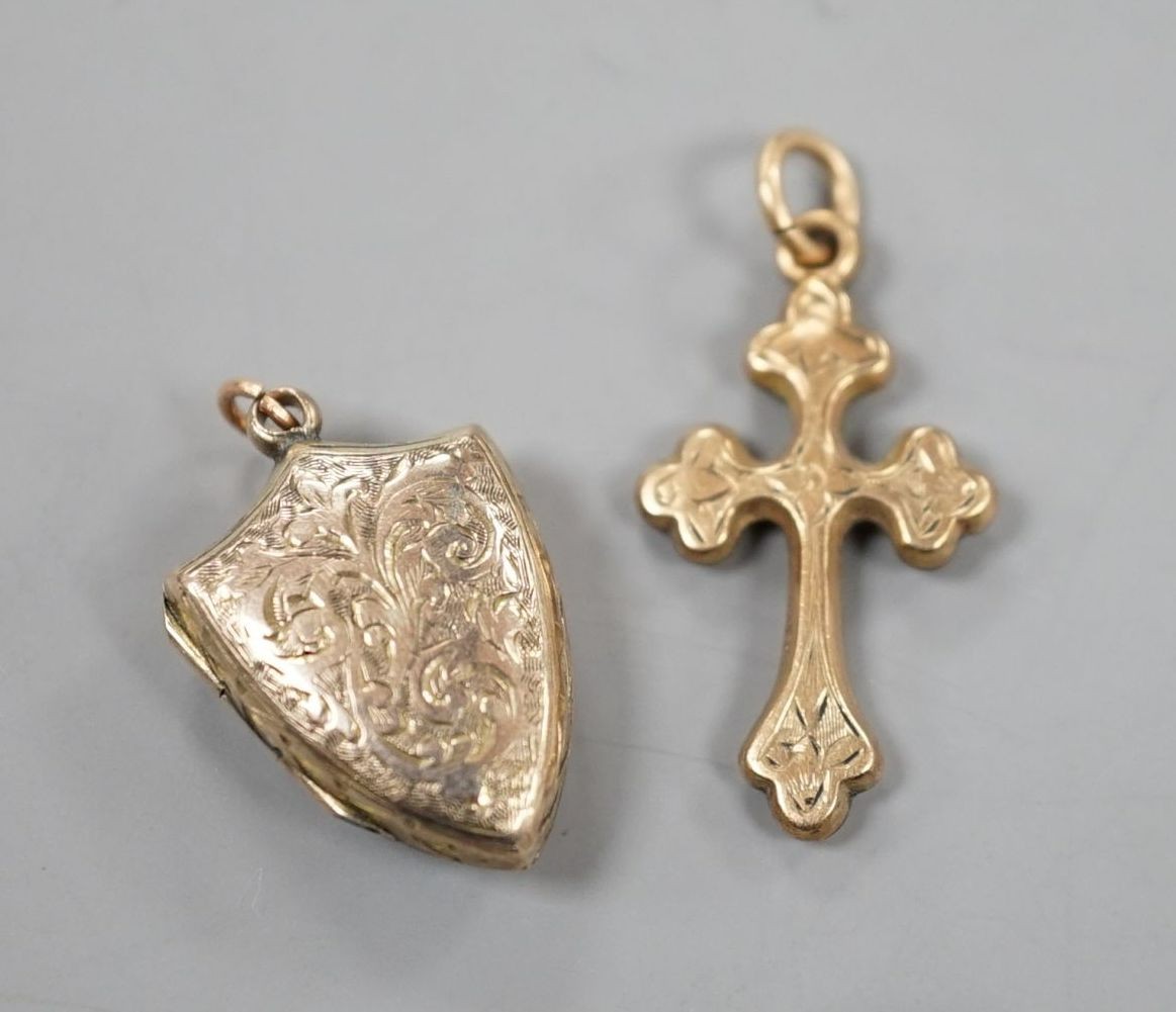 A 9ct gold cross pendant charm, 21mm and a similar engraved yellow metal shield shaped locket charm